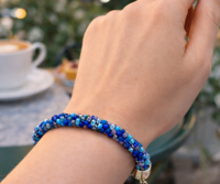 Handmade blue Kumihimo bracelet worn at café table, Caribbean Blue glass seed beads, adjustable clasp artisan jewelry